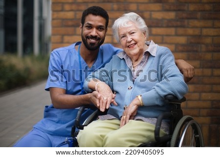 Happy senior woman at wheelchair spending time outside with her assistant. Royalty-Free Stock Photo #2209405095