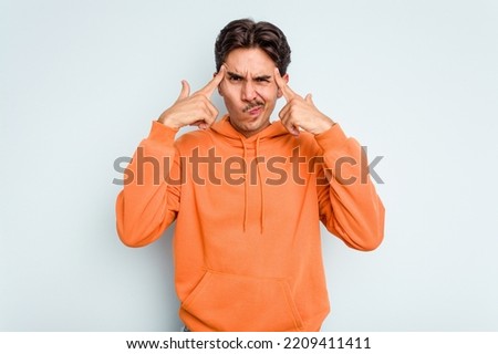 Young hispanic man isolated on blue background focused on a task, keeping forefingers pointing head.