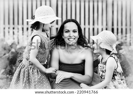 A family picture of a smiling mother together with her two happy daughters on either side of her.  Processed in black and white. 