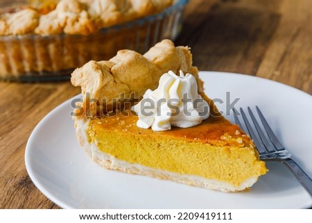 Close-up of a slice of Pumkin Pie on a white plate with fork, and a dollop of cream on the top.  Royalty-Free Stock Photo #2209419111
