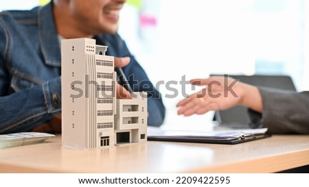 A modern building or condominium model is on a table with blurred background of a client meeting with a female realtor or broker. cropped and close-up image Royalty-Free Stock Photo #2209422595