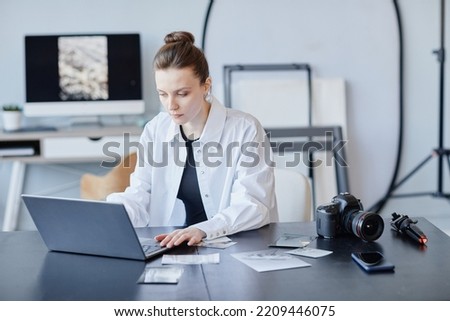 Portrait of young female photographer using laptop for retouch and photo editing in minimal studio setting, copy space