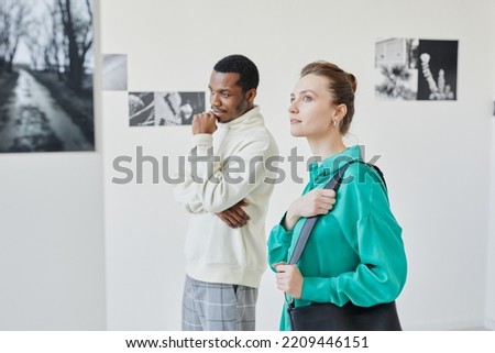 Side view portrait of elegant young woman looking at art in gallery or museum and smiling with inspiration, copy space
