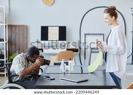 Side view portrait of young black man with disability as photographer taking pictures in studio with assistance