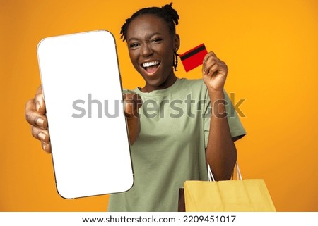 Smiling young girl holds smart phone and credit card in yellow studio