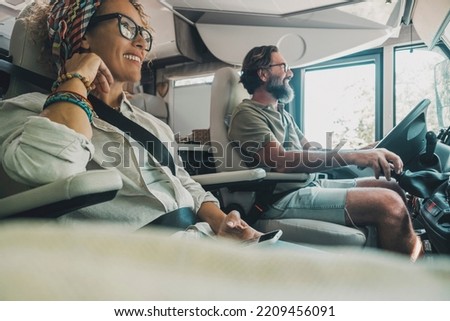 Side view of happy traveler couple inside camper van rv vehicle driving and enjoying road trip vacation or of grid vanlife lifestyle. People and transport concept. Man and woman travel on motor home Royalty-Free Stock Photo #2209456091