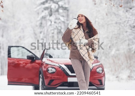 Cheerful emotions. Beautiful young woman is outdoors near her red automobile at winter time.