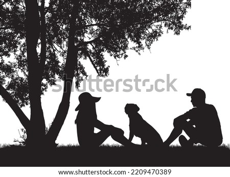 A couple of people with a dog are sitting under a tree.