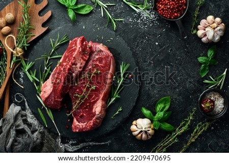 Raw juicy striploin steak. Fermented steak with rosemary and spices is ready for cooking. Meat. On a black stone background. Top view. Royalty-Free Stock Photo #2209470695