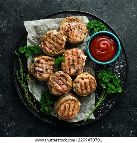 Grilled medallions wrapped in bacon. in a pan, ready to eat. On a black concrete background. Top view.