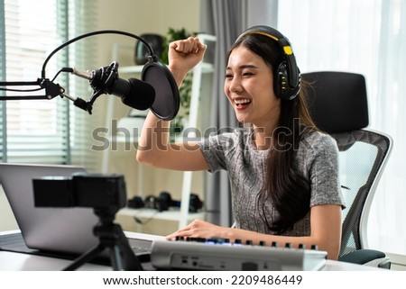 Asian attractive audio DJ woman speaks into microphone to broadcasting. Young beautiful female blogger influencer wearing headphones and recording morning news podcast show for radio at home studio.