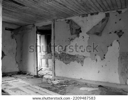 An open dilapidated and peeling door viewed through a another door frame from inside of an old abandoned room with peeling paint crumbling plaster and warped floor boards Royalty-Free Stock Photo #2209487583