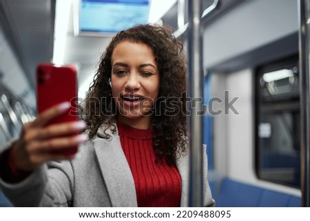 smiling woman taking a selfie while standing on a subway train .