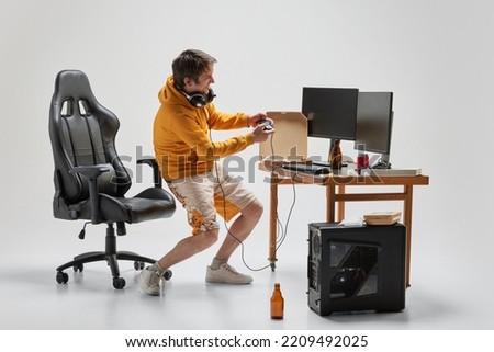 Gambler. Emotional man, student sitting at home, playing computer games isolated over grey background. Business, studying, education, youth, remote workplace concept. Copy space for ad, text