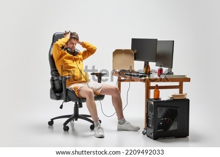 Stress. Emotional man, student sitting at home, playing computer games isolated over grey background. Business, studying, education, youth, remote workplace concept. Copy space for ad, text