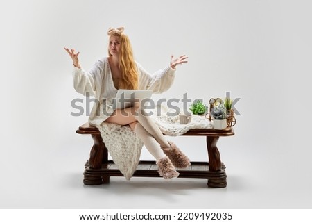 Despair. Young beautiful girl sitting at wooden table and using laptop isolated over grey background. Ideas, inspiration, imagination. Retro, vintage style. Copy space for ad