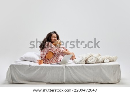 Love, dreams. Young beautiful girl in home wear sitting on bed at home and dreaming isolated on gray background. Ideas, inspiration, imagination. Art, beauty, youth