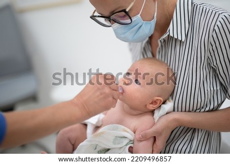 Pediatrician administring oral vaccination against rotavirus infection to little baby in presence of his mother. Children health care and disease prevention Royalty-Free Stock Photo #2209496857