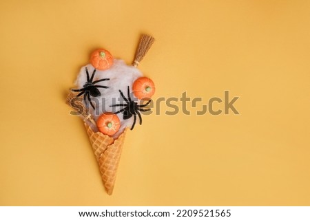 Halloween icecream made with ice-cream cone, spider web, witch's broom and pumpkins on orange background. Halloween sweet dessert. Flat lay, copy space