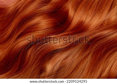 Red hair close-up as a background. Women's long orange hair. Beautifully styled wavy shiny curls. Hair coloring bright shades. Hairdressing procedures, extension. Royalty-Free Stock Photo #2209524295
