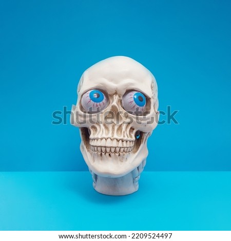 Realistic human skull with bright blue eyes making silly face. Funny spooky Halloween composition.