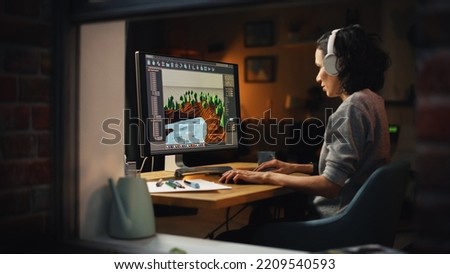 Female Video Game Designer Works on a New 3D Level on Personal Computer. Focused Woman Creating Metaverse and Design Video Game. Shot Into the Apartment Window Late at Night. Royalty-Free Stock Photo #2209540593