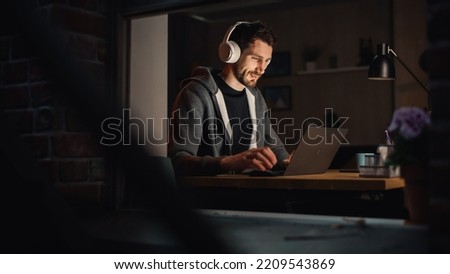 Happy Software Developer Working on a Laptop. Cheerful Information Technology Specialist Wearing Headphones, Listens to Music, Does Professional Work. Remote Job at Home Office Concept. Royalty-Free Stock Photo #2209543869