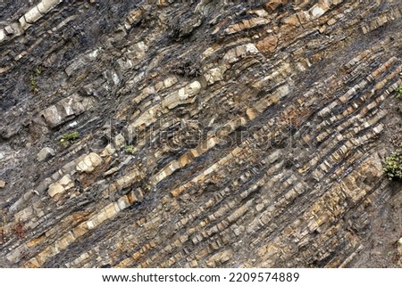 Diagonal striations in a rocky hillside show a geological history of land movement and sediment deposits. Royalty-Free Stock Photo #2209574889