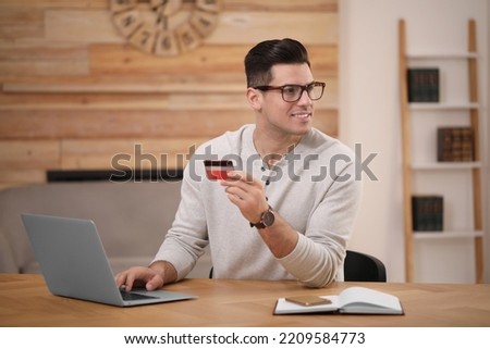Man using laptop and credit card for online payment at desk in room