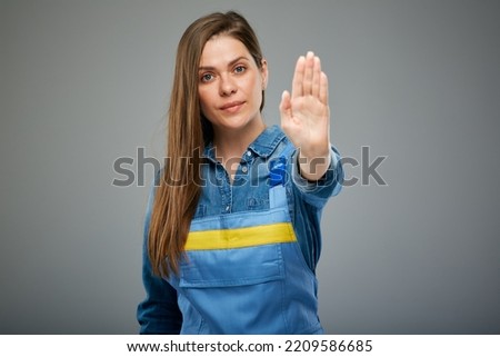 Woman in blue overalls showing stop sign. Isolated female portrait in builder worker uniform.