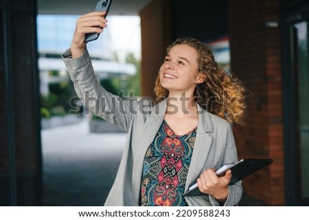 Happy attractive young woman student with laptop and books taking selfie with mobile phone outdoors. Beautiful portrait. People lifestyle. Smart city.