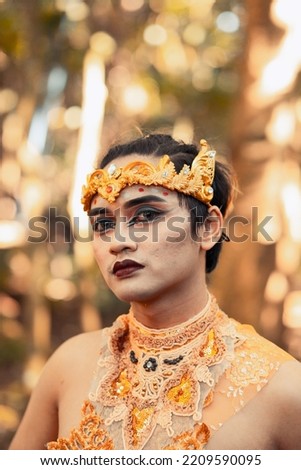 Asian men wearing black eyeshadow and red black lips on her face while wearing a gold crown on the head inside the village