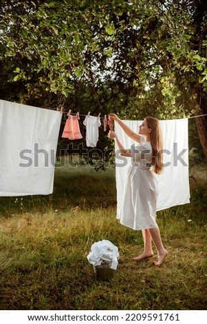 a pregnant girl in a white dress hangs children's underwear in the garden