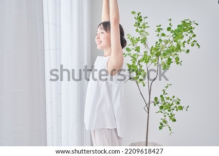 A woman taking a deep breath by a bright window Royalty-Free Stock Photo #2209618427