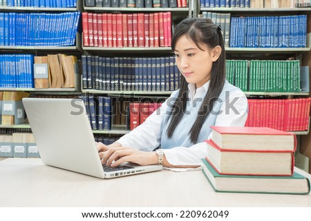 Asian female student typing on notebook in library