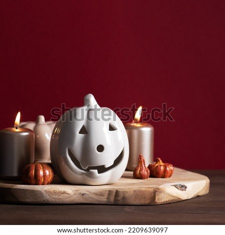 Autumn home decor with ceramic pumpkins, burning candles. Cozy scandinavian style still life with fall decoration in dark red colors