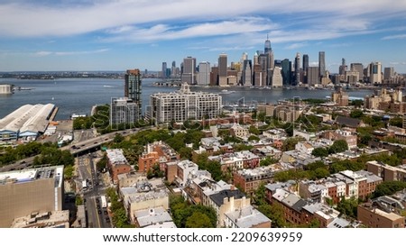An aerial view of Brooklyn, NY on a beautiful day with blue skies and white clouds. The New York City skyline is in the background featuring the Freedom Tower and lower Manhattan.