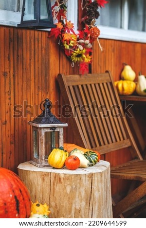 Autumn halloween decoration with lantern and pumpkin on tree trunk next wooden cabin. Garden furniture at patio