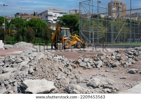 New park construction for children site next to the football pitch in the city, yellow excavator demolished old structure on a sunny day. freeing up space for new park construction
