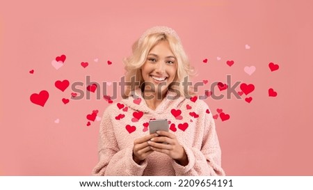 Happy pretty young blonde woman using cell phone, texting her boyfriend online or using dating mobile app while standing over pink background, red hearts around, studio shot, collage