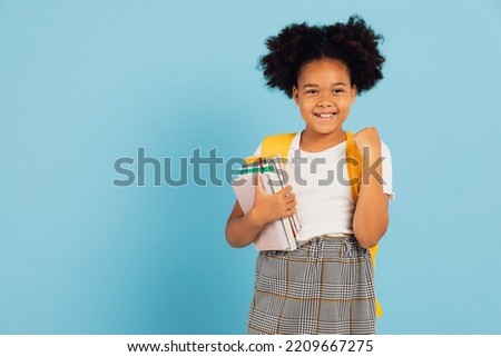 Happy African American schoolgirl pointing cool on blue background, back to school concept.