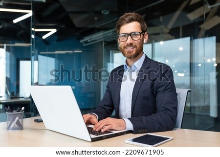 Portrait of mature boss inside office with laptop, successful and satisfied investor manager looking at camera and smiling man in glasses and business suit, investor with beard sitting on chair. Royalty-Free Stock Photo #2209671905