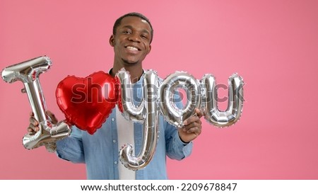 Smiling African-American teenager calls for love or confesses his love to loved one, holds word I love you from helium balloon in his hands, congratulates on Mother Day or Valentines Day.