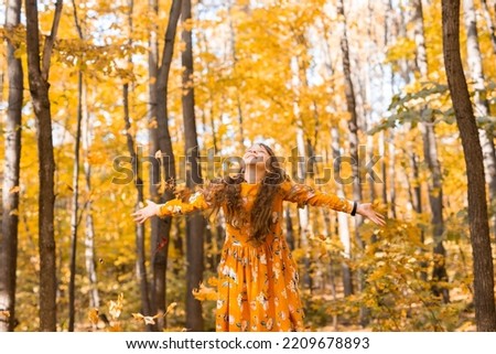 Child girl throwing fall leaves on autumn nature - fun, leisure and childhood concept
