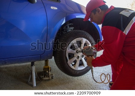 Picture of a mechanic in his workshop who with a pneumatic screwdriver disassembles the wheel of a car resting on trestles. Car repair work
