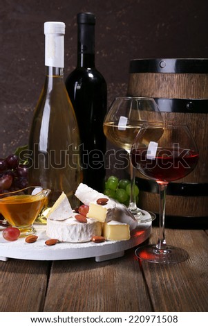 Supper consisting of Camembert cheese, honey, wine and grapes on stand and wine barrel on wooden table on brown background