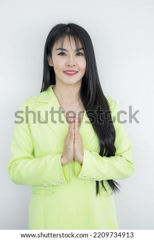 Asian working Thai business woman wearing green pastel suit made hello gesturing Sawasdee and smiling, Thai culture friendly greeting, Sawasdee symbol from Thailand greeting culture identity.