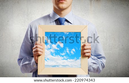 Young smiling businessman holding wooden frame with sky picture