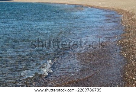photo of sea shore and large rocks in it, foamy waves crashing on shore, reflected sunlight, yellow moss boulders