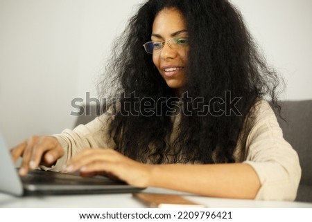 Happy black woman typing text on computer. Cheerful dark skinned female working on laptop at home. Download royalty free image of African entrepreneur person doung work. Stock photo of freelancer